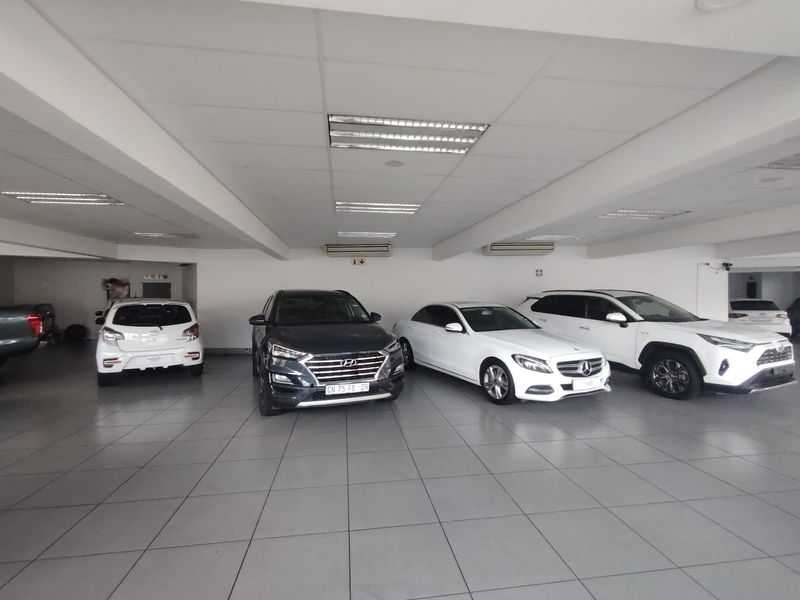 Spacious indoor showroom or garage area featuring tiled flooring, recessed ceiling lighting, and wall-mounted air conditioning units.