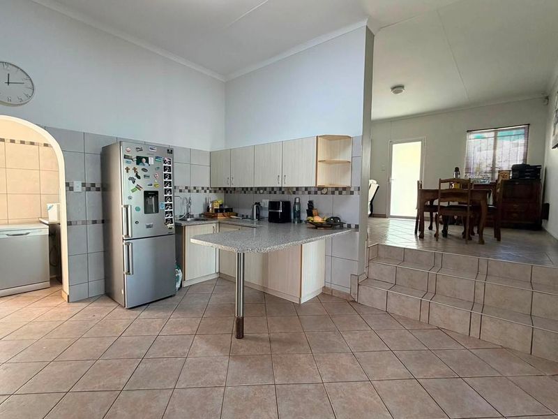 Kitchen featuring built-in cabinetry, laminate countertops, and tiled flooring, with an open-plan layout leading to a raised dining area through an archway.