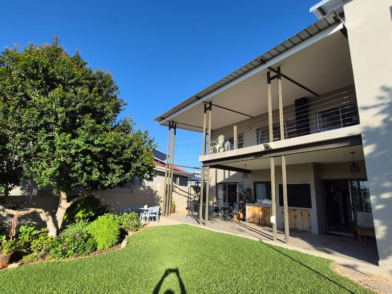 A spacious rear exterior view featuring a two-story home with a covered ground-floor patio, an upper-level balcony, and a well-maintained garden.