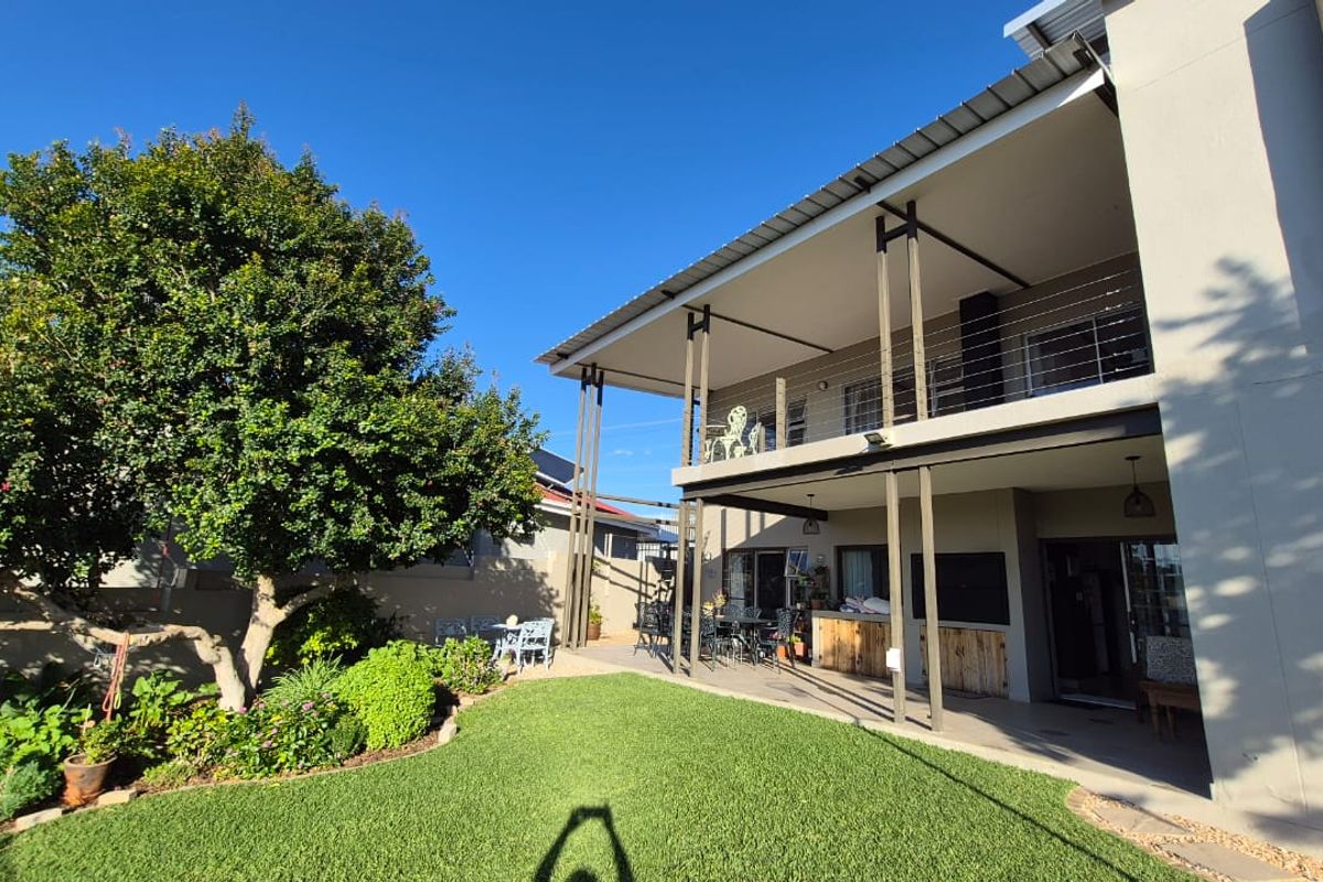 A spacious rear exterior view featuring a two-story home with a covered ground-floor patio, an upper-level balcony, and a well-maintained garden.