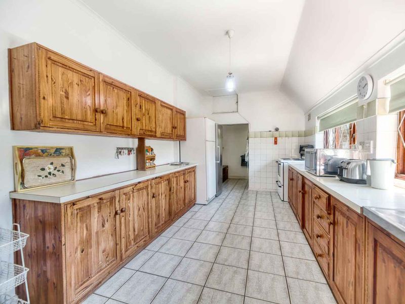 A functional galley-style kitchen featuring extensive wooden cabinetry, tiled flooring, and a tiled backsplash, offering a classic layout with ample storage space.