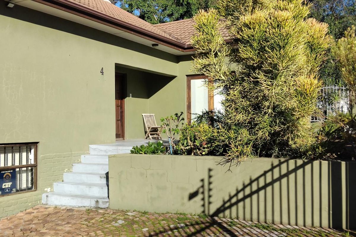 Front exterior view of the apartment building featuring a paved driveway, concrete entrance steps, and a low boundary wall with established garden landscaping.