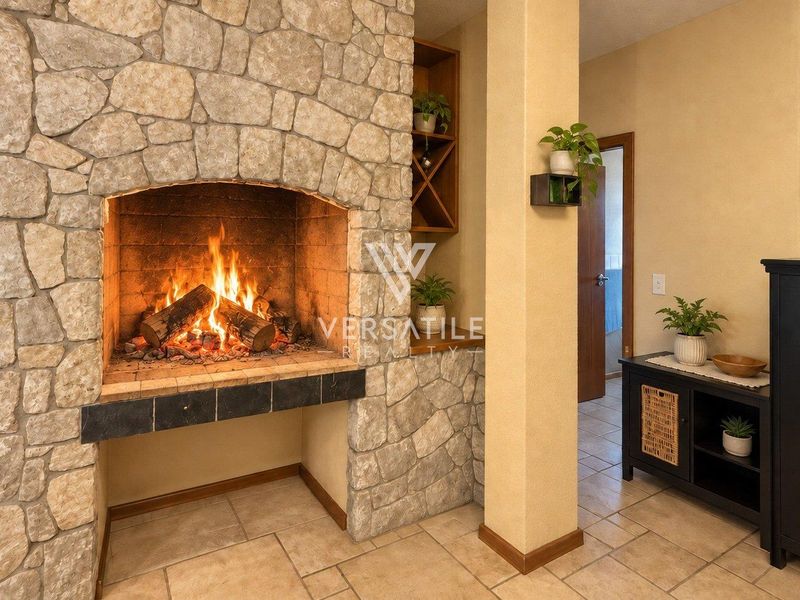 A cozy living room featuring a prominent stone fireplace with a built-in hearth and integrated shelving, complemented by neutral tiled flooring.
