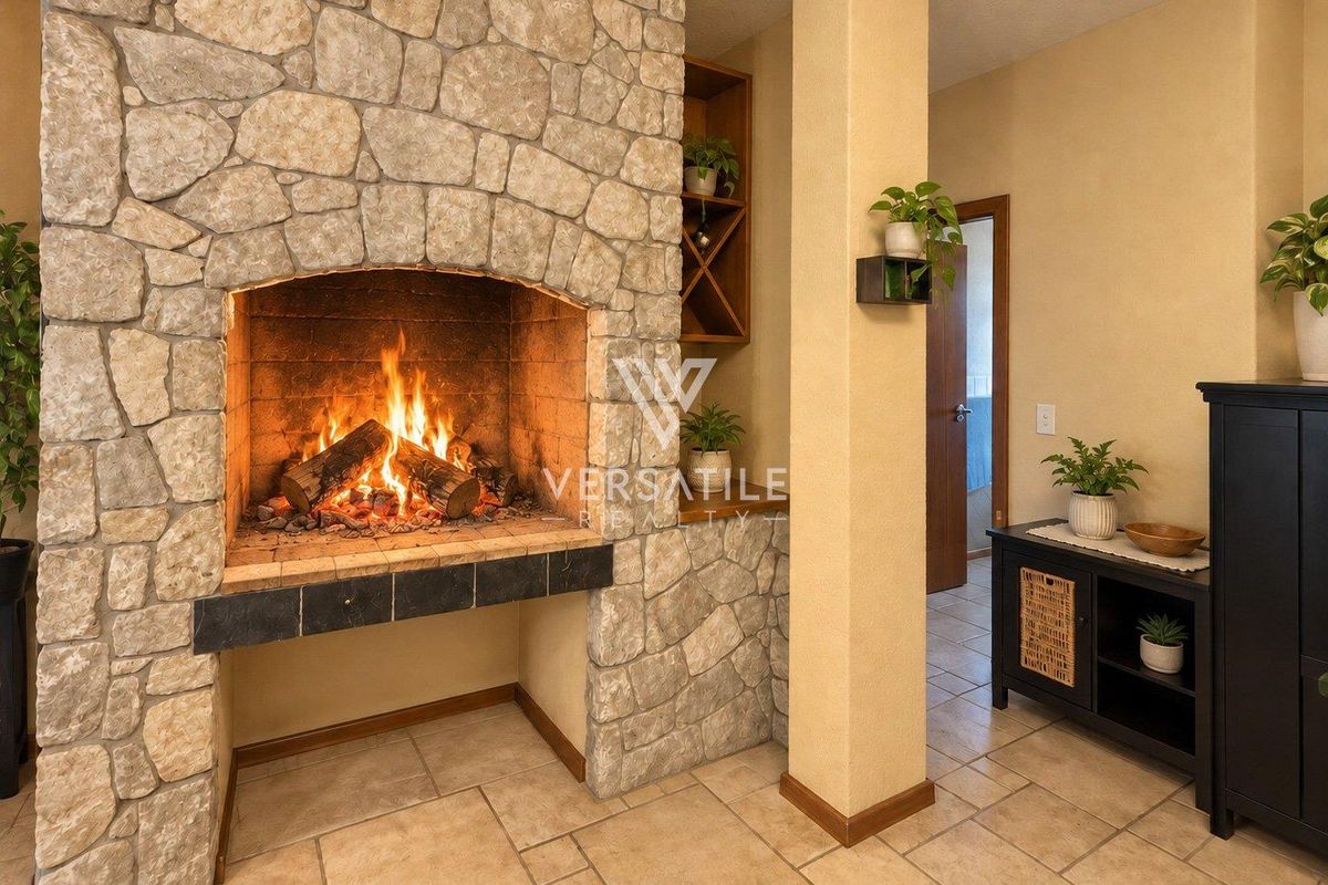 A cozy living room featuring a prominent stone fireplace with a built-in hearth and integrated shelving, complemented by neutral tiled flooring.
