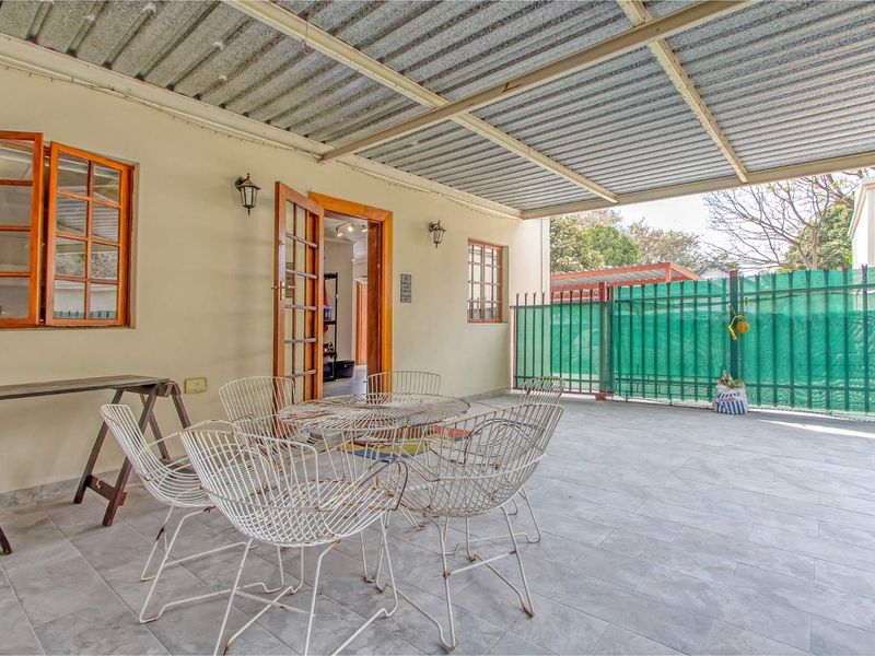 A covered outdoor patio featuring tiled flooring, a corrugated metal roof, and direct access to the interior through timber-framed glass doors.