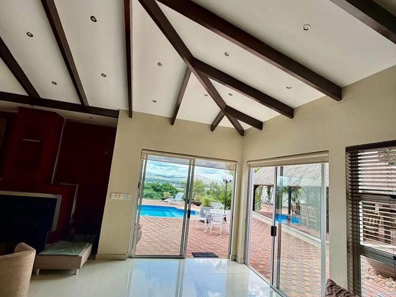 Spacious living room featuring high vaulted ceilings with exposed timber beams, tiled floors, and large sliding doors providing seamless access to the pool area.