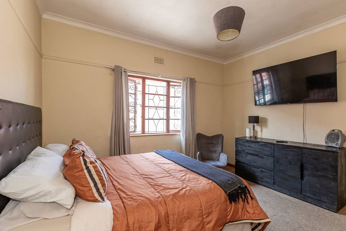 A bedroom featuring carpeted flooring, coving, and a metal security window grille, with wall-mounted television and neutral wall finishes.