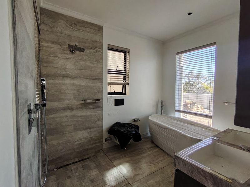 Modern bathroom featuring a walk-in shower, freestanding bathtub, and dual vanity with contemporary tile finishes and large windows.