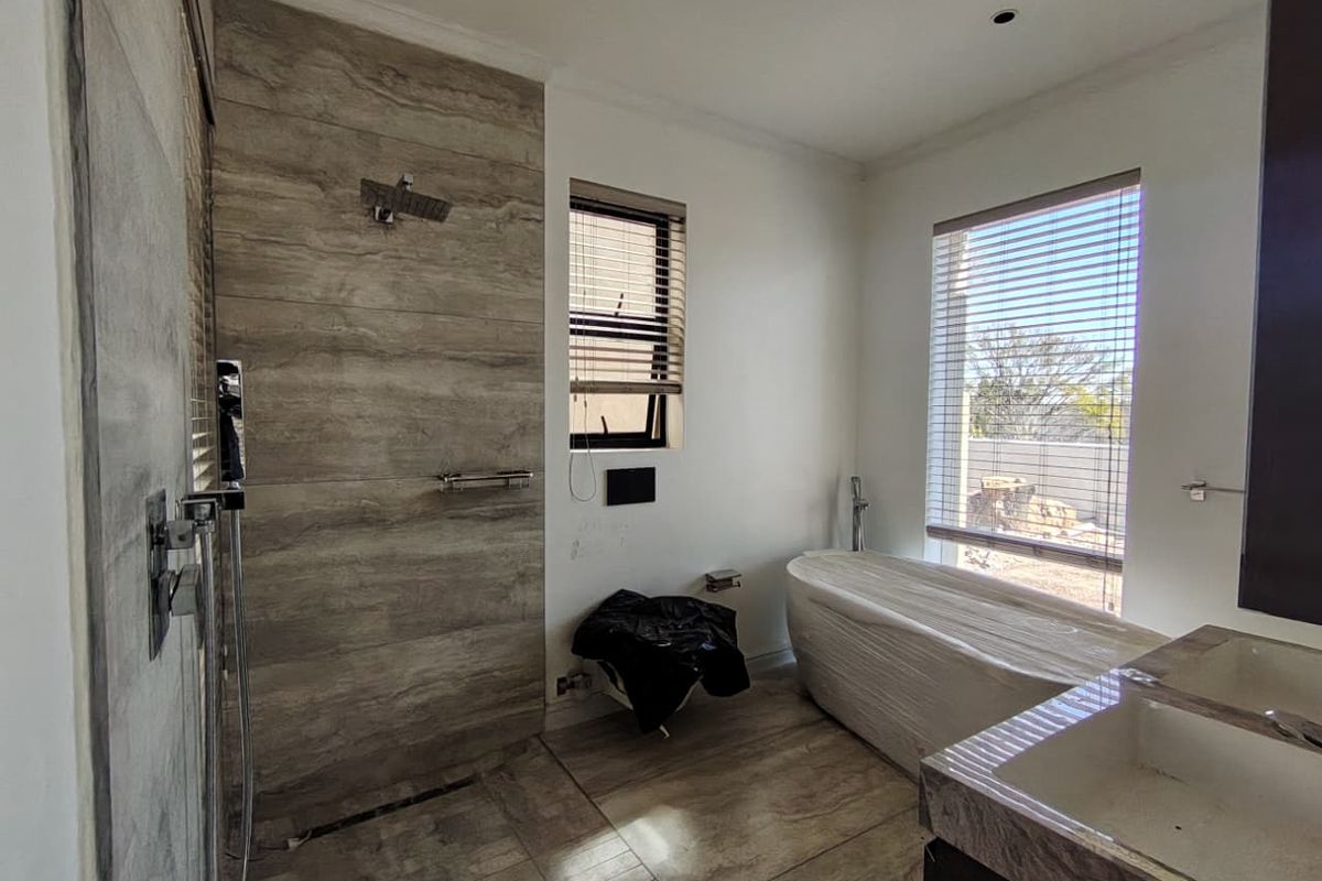Modern bathroom featuring a walk-in shower, freestanding bathtub, and dual vanity with contemporary tile finishes and large windows.