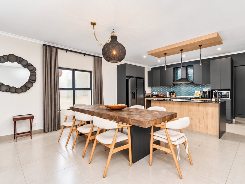 Modern open-plan kitchen and dining area featuring sleek dark cabinetry, a wooden kitchen island, tiled backsplash, and contemporary lighting fixtures.