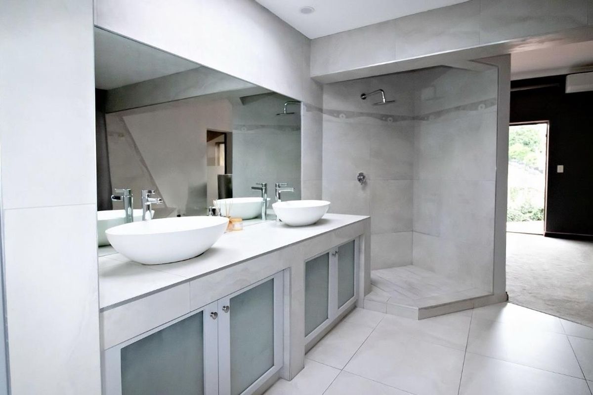 Modern bathroom featuring a double vanity with vessel sinks, large wall-to-wall mirror, and a spacious walk-in shower with tiled finishes.