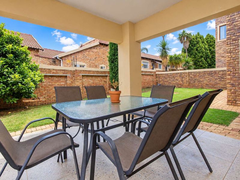 A covered patio area featuring paved flooring and a private garden enclosed by brick boundary walls with electric fencing.