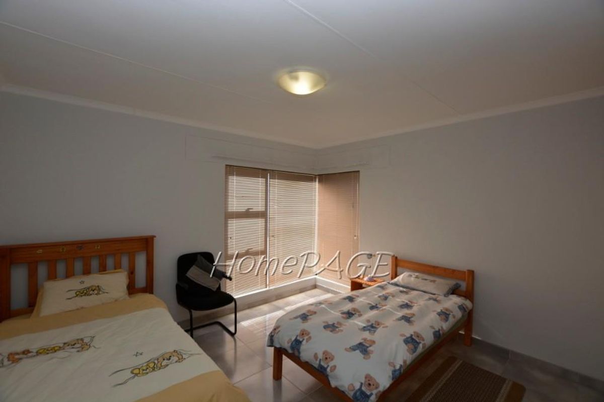 A functional bedroom featuring tiled flooring, neutral wall finishes, and corner windows fitted with horizontal blinds.
