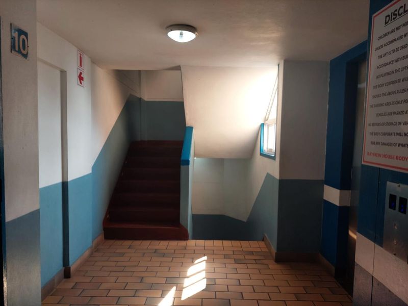A functional apartment building hallway featuring a staircase, elevator access, and tiled flooring with standard wall finishes.