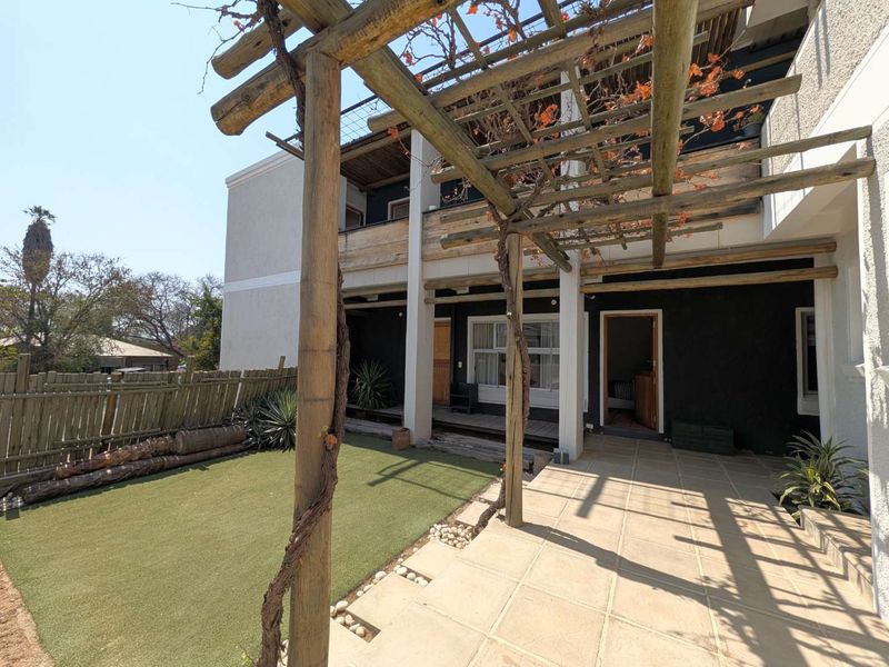 Rear exterior view featuring a timber pergola, tiled patio area, and artificial lawn, providing a functional outdoor space for the guest house.