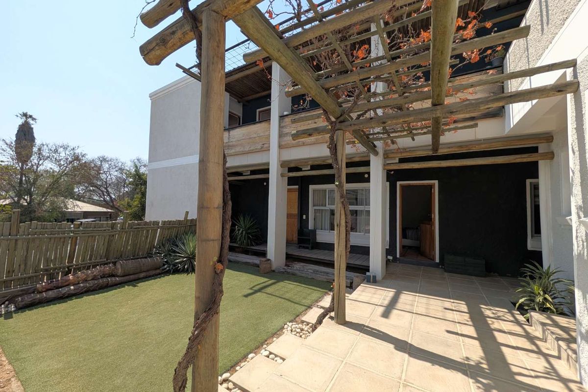 Rear exterior view featuring a timber pergola, tiled patio area, and artificial lawn, providing a functional outdoor space for the guest house.