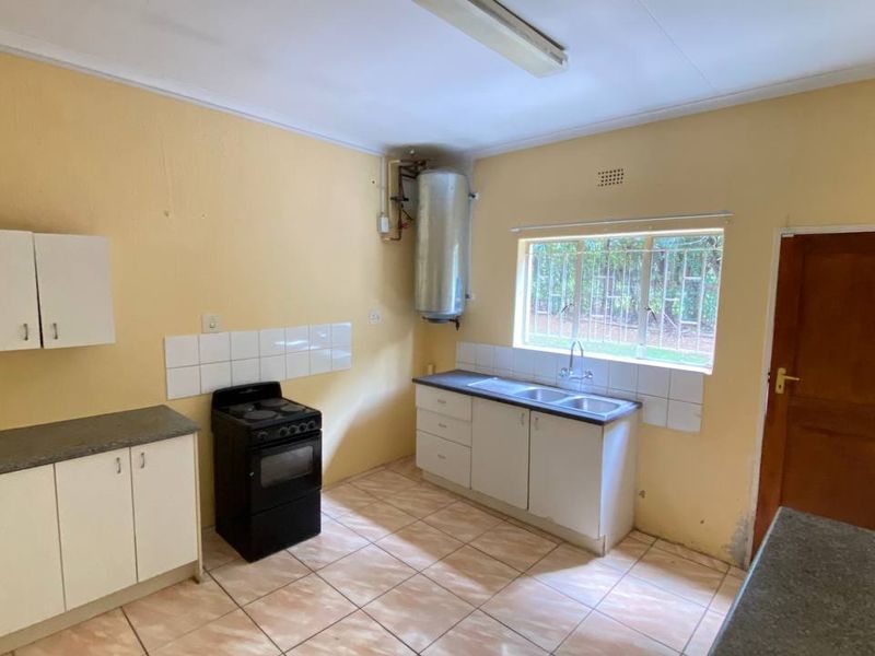 A functional kitchen featuring tiled flooring, built-in cabinetry, a double sink, and a freestanding stove, offering potential for modernization and cosmetic updates.