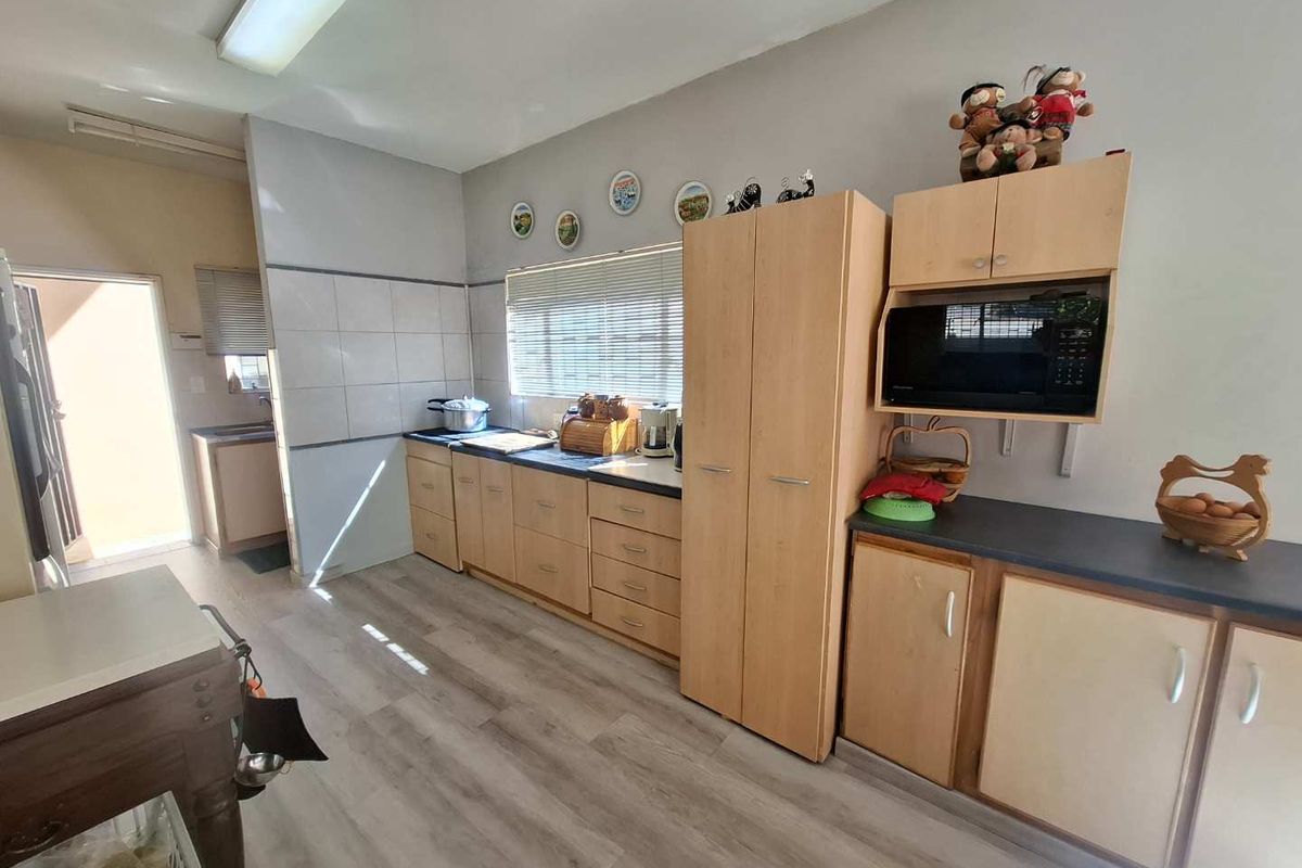 A functional kitchen featuring light wood-tone cabinetry, dark countertops, tiled splashbacks, and durable laminate flooring with natural light from the window.