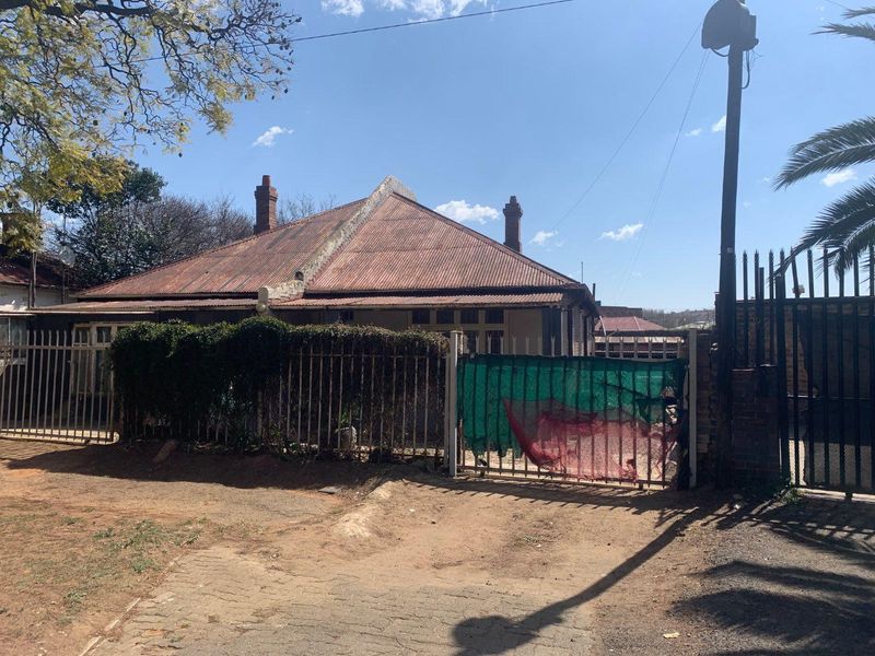Front exterior view of a single-story house featuring a corrugated iron roof, brick chimneys, and metal security fencing.