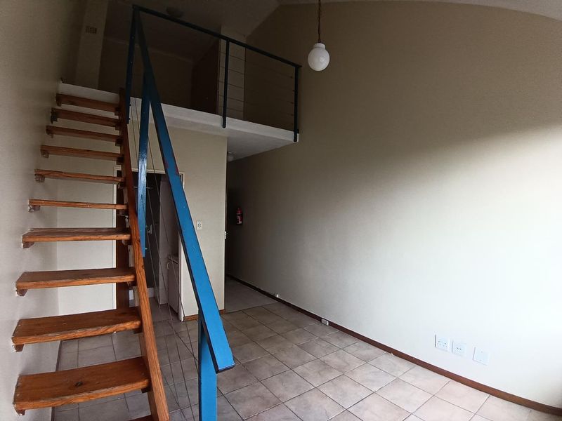 Open-plan living area featuring a mezzanine level, timber staircase with metal balustrade, and neutral tiled flooring.