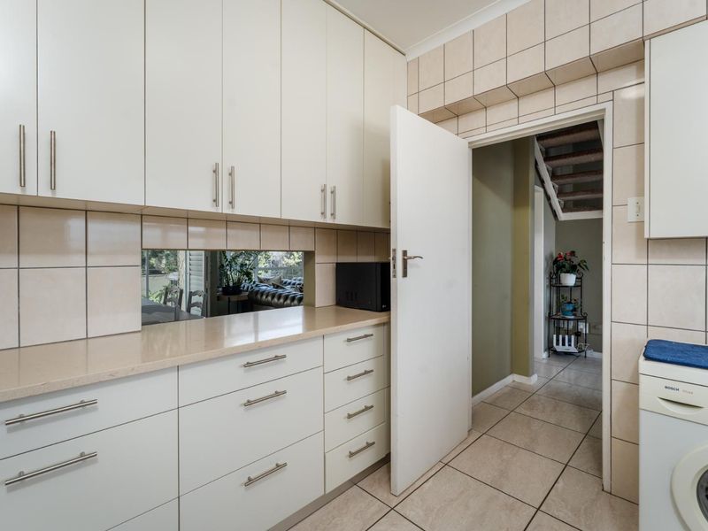 A functional scullery featuring ample built-in cabinetry, stone countertops, tiled splashbacks, and a dedicated space for laundry appliances.