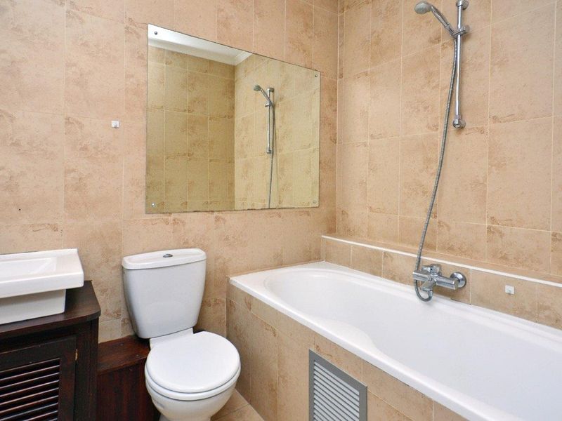 A functional bathroom featuring tiled walls, a bathtub with a handheld shower attachment, a toilet, and a wall-mounted basin.