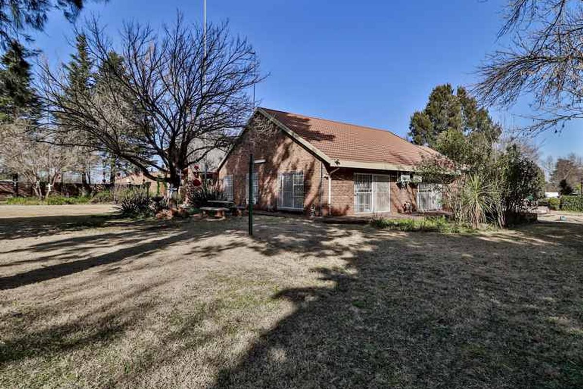 Rear view of the brick farmhouse featuring a tiled roof, security-fitted windows, and access to the surrounding garden area.