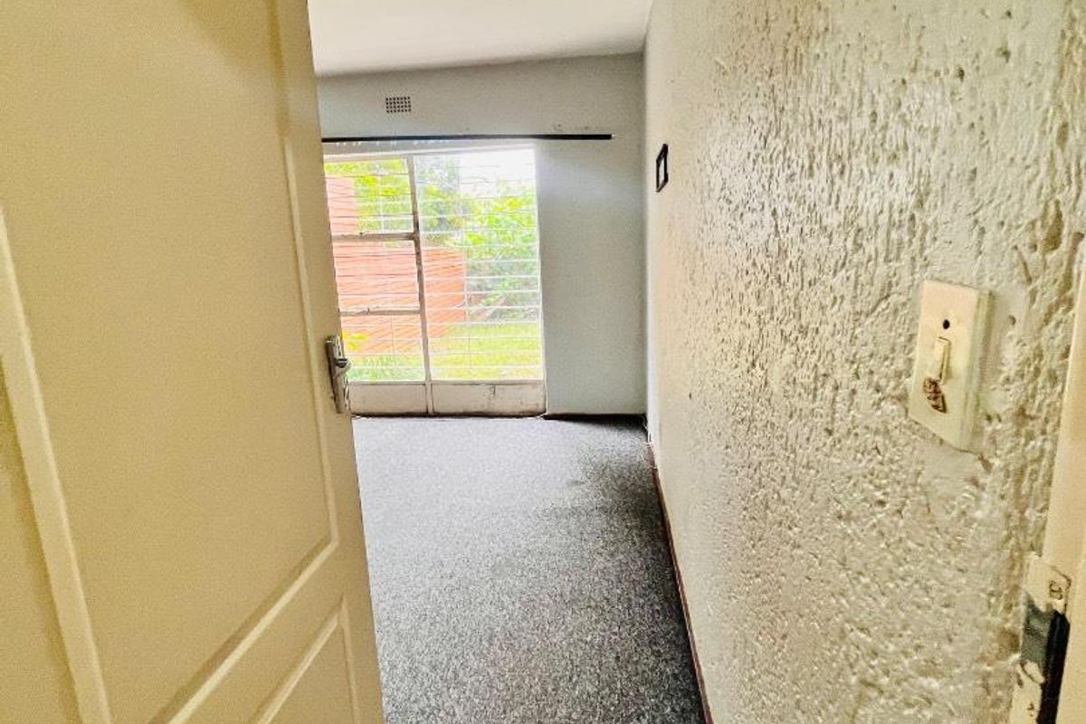 A view into an empty bedroom featuring textured walls, carpeted flooring, and a large window providing natural light.