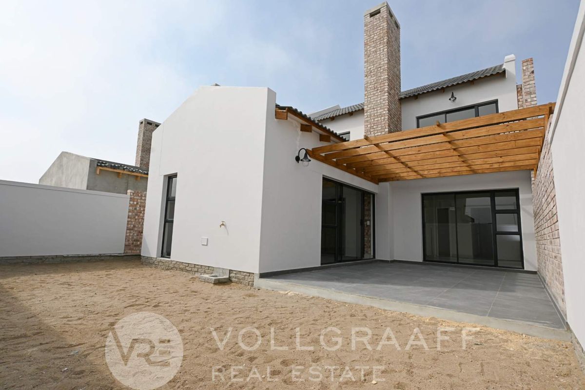Rear view of the townhouse featuring a covered patio with a wooden pergola, brick chimney, and sliding glass doors leading to an unlandscaped garden area.