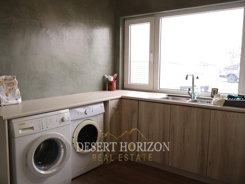 A functional laundry room featuring modern laminate cabinetry, a stainless steel double sink, and a durable countertop with space for under-counter appliances.