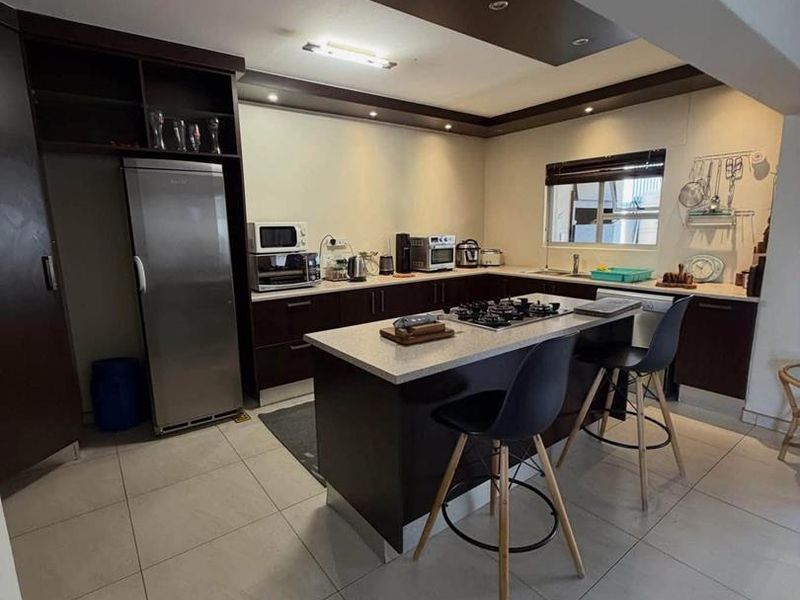 Modern kitchen featuring a central island with a gas hob, dark wood cabinetry, stone countertops, and recessed ceiling lighting.
