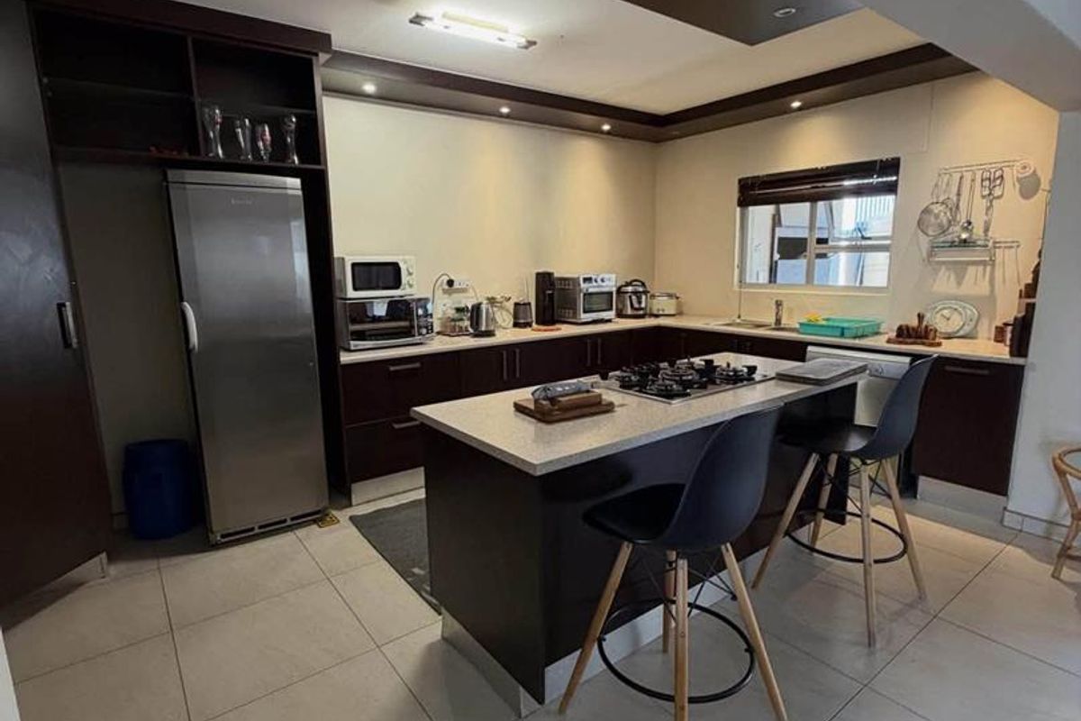 Modern kitchen featuring a central island with a gas hob, dark wood cabinetry, stone countertops, and recessed ceiling lighting.
