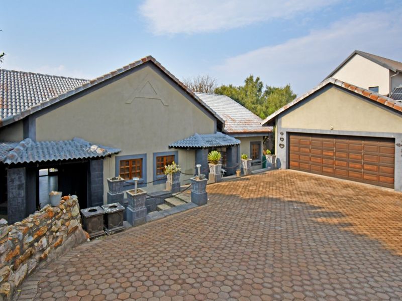 Front exterior view of the property featuring a paved driveway, double garage with timber doors, and a stone retaining wall.