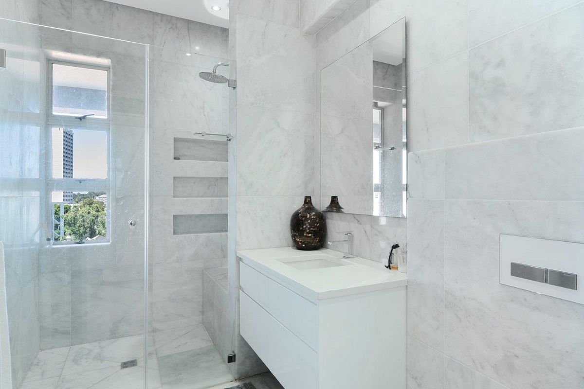 Modern bathroom featuring floor-to-ceiling marble tiling, a floating vanity, a frameless glass shower with a built-in niche, and high-end fixtures.