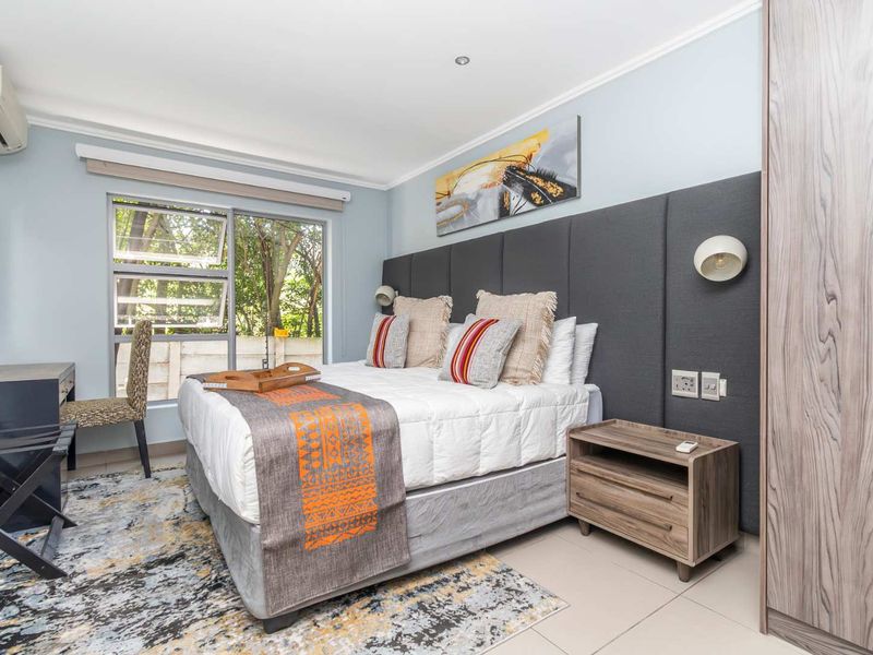 A well-maintained bedroom featuring a large upholstered headboard, built-in wardrobe, tiled flooring, and a wall-mounted air conditioning unit.