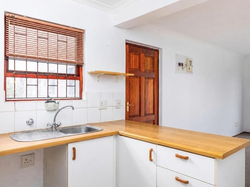 A functional kitchen area featuring white cabinetry, laminate countertops, a stainless steel sink, and a timber door, offering a clean and practical layout.