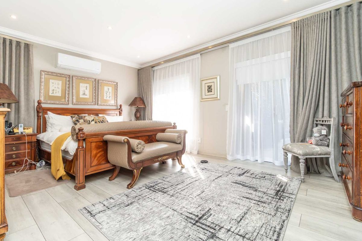 Spacious bedroom featuring light-toned tiled flooring, recessed ceiling lighting, a wall-mounted air conditioning unit, and large sliding glass doors with floor-to-ceiling curtains.