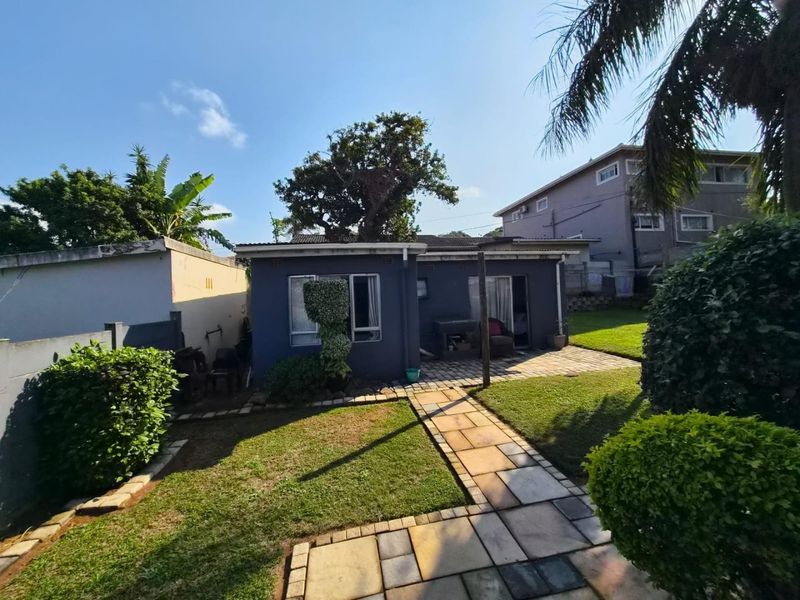 Rear view of the property featuring a paved walkway, established lawn, and boundary walls.