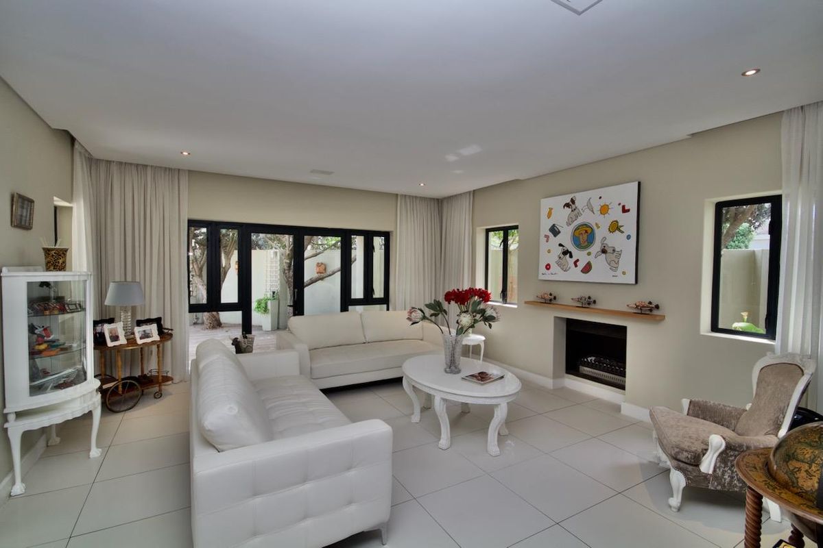 A bright and spacious living room featuring large windows, tiled flooring, and a built-in fireplace with a wooden mantelpiece.