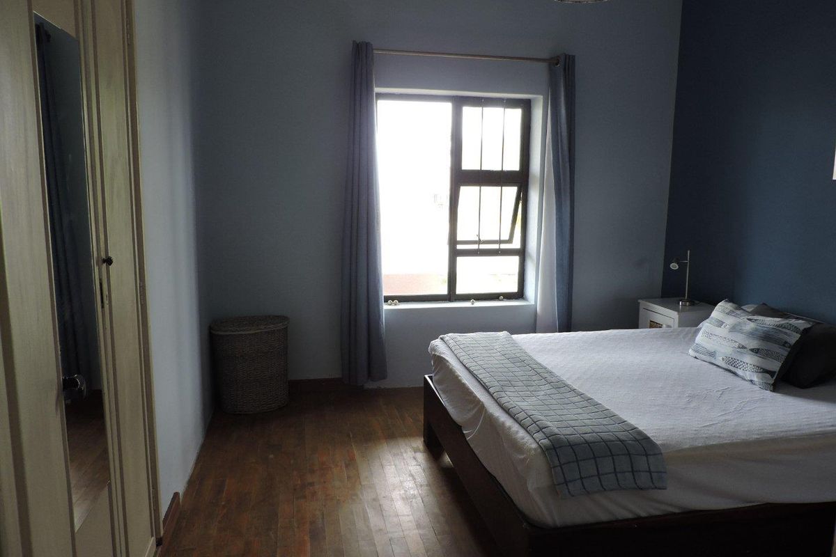 A bedroom featuring timber flooring, built-in wardrobe cabinetry, and a window with security bars.
