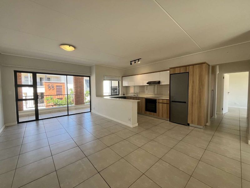 An open-plan living and kitchen area featuring modern cabinetry, integrated appliances, and large sliding doors leading to a balcony with neutral tiled flooring throughout.