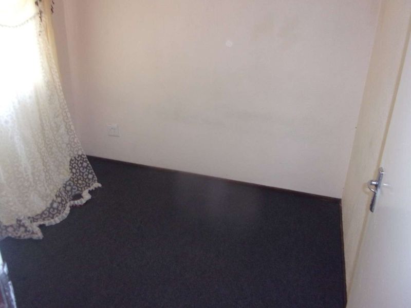 A small, empty bedroom featuring dark flooring and plain walls, suitable for a compact sleeping area or home office.