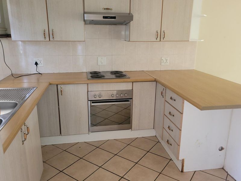 A functional kitchen featuring laminate cabinetry, built-in oven, electric hob, extractor fan, and tiled flooring. The space is clean and ready for updates.