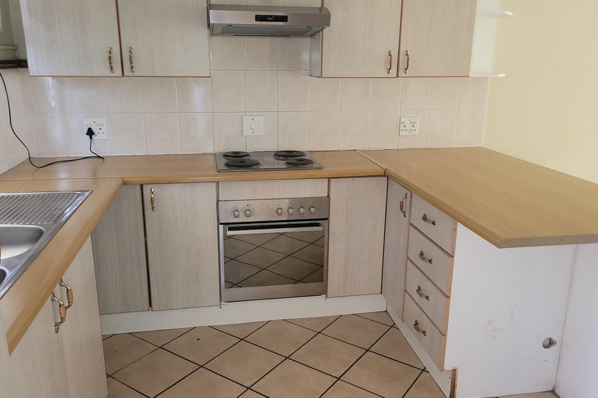 A functional kitchen featuring laminate cabinetry, built-in oven, electric hob, extractor fan, and tiled flooring. The space is clean and ready for updates.