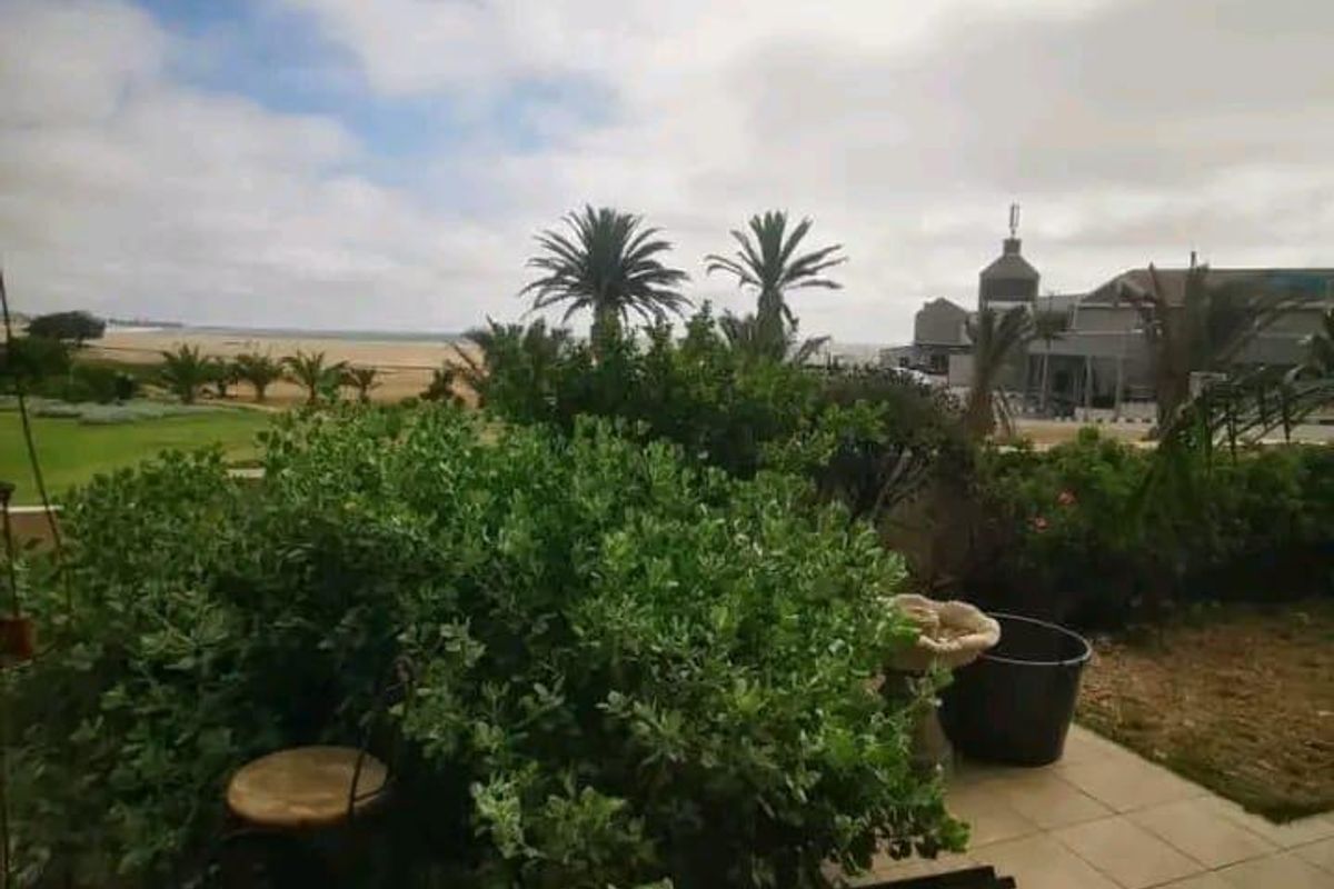A view from a patio overlooking a coastal garden and surrounding landscape, featuring tiled flooring and established greenery.