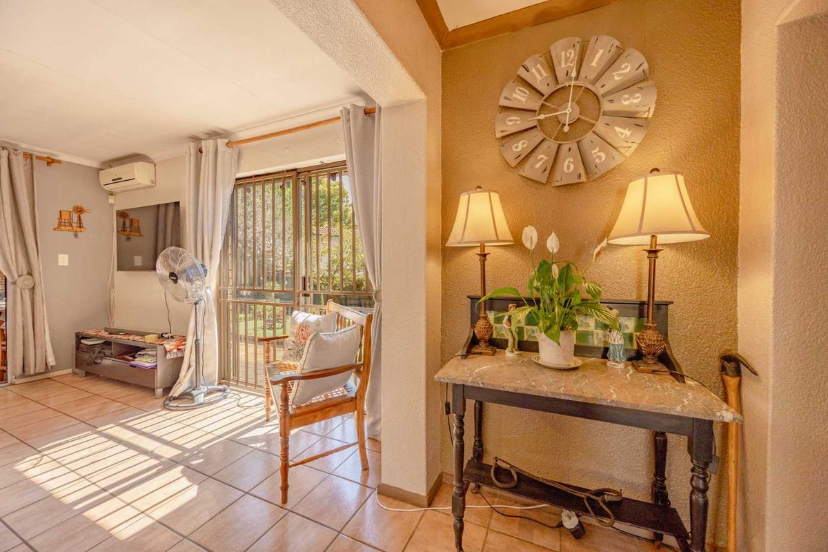 A living area featuring tiled flooring, a wall-mounted air conditioning unit, and a sliding door with security gate leading to the exterior.