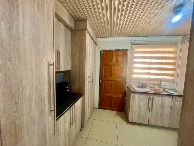 A functional kitchen featuring wood-look cabinetry, laminate countertops, a stainless steel sink, and tiled flooring with a textured ceiling finish.