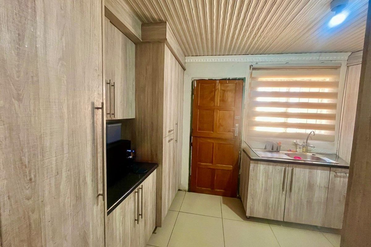 A functional kitchen featuring wood-look cabinetry, laminate countertops, a stainless steel sink, and tiled flooring with a textured ceiling finish.