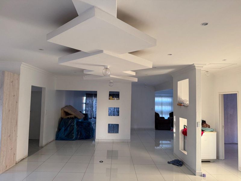 Spacious open-plan living area featuring a modern tiered ceiling design, recessed wall niches, and neutral tiled flooring throughout.