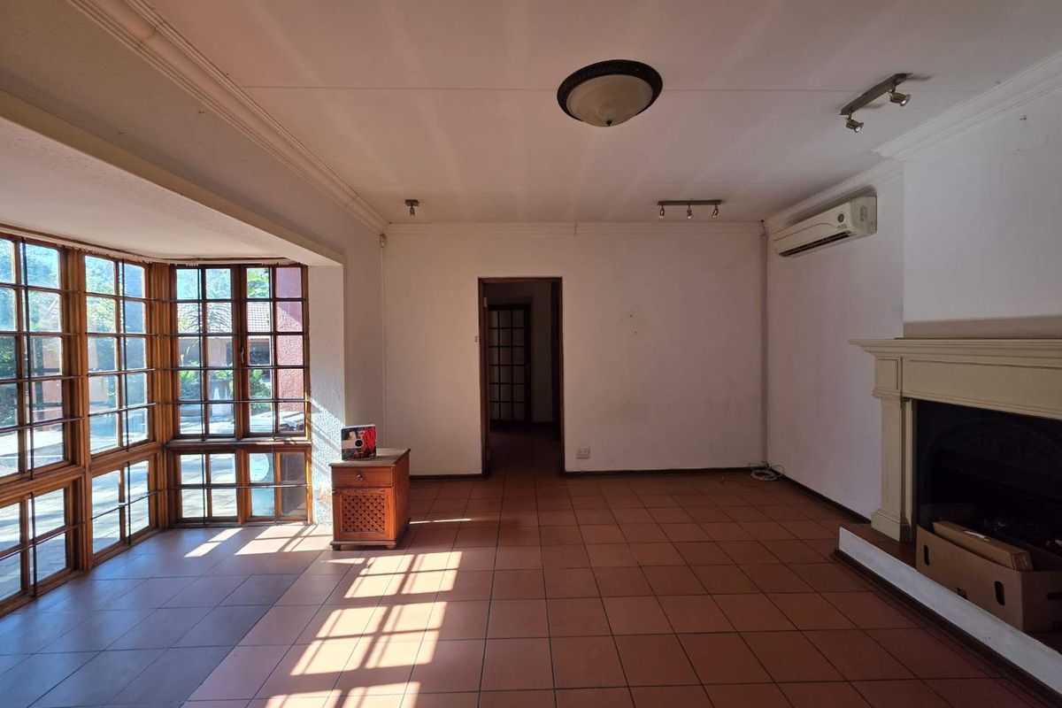 Spacious living room featuring large wooden-framed bay windows, tiled flooring, a built-in fireplace, and a wall-mounted air conditioning unit.